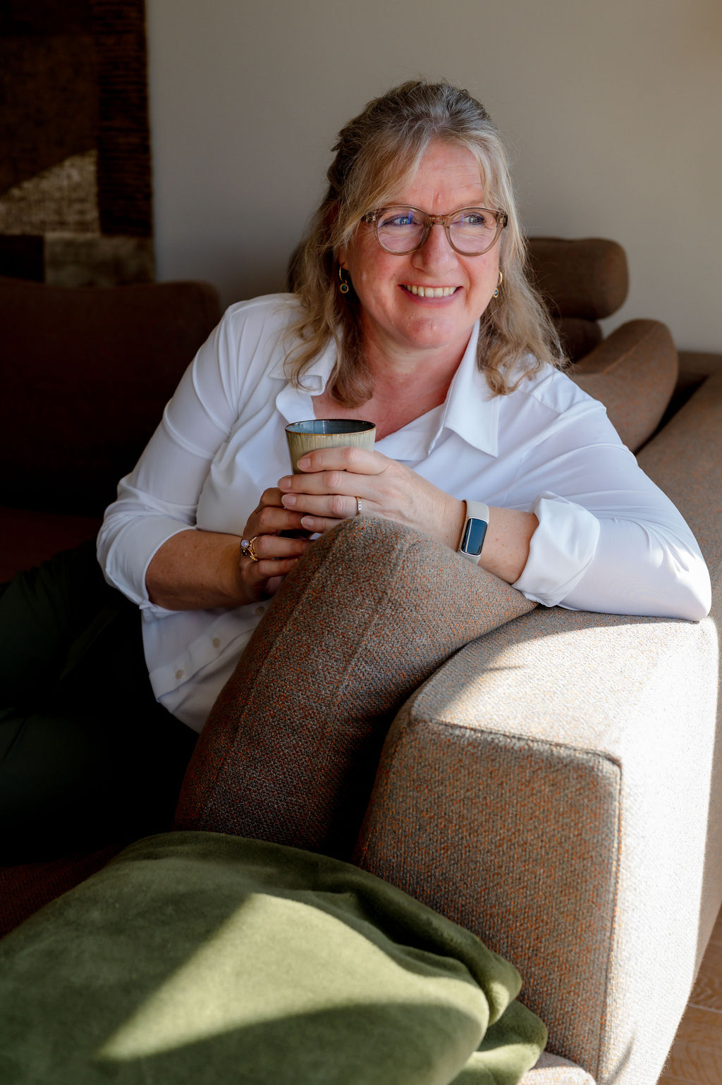 Susanne Papen lachend met een kopje koffie op de bank naar buiten kijkend