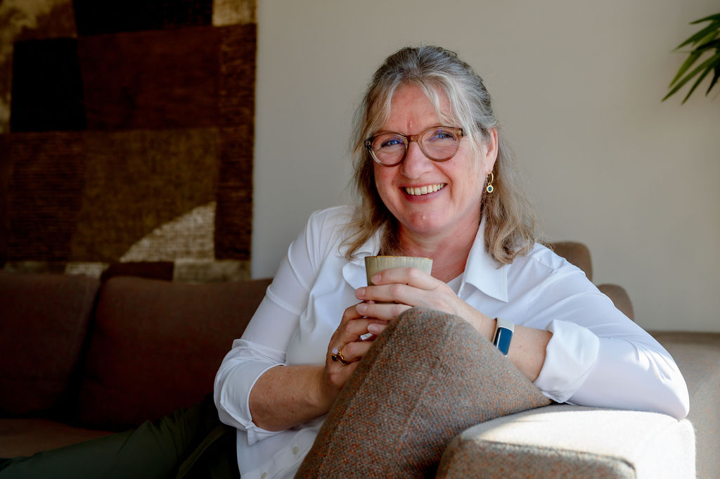Susanne Papen lachend met een kopje koffie op de bank naar buiten kijkend
